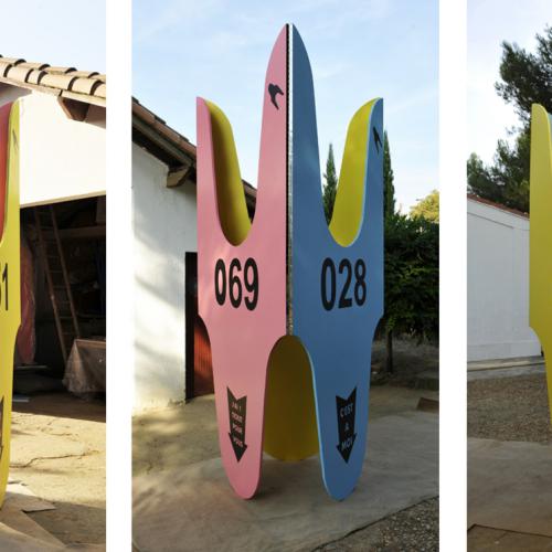 Sculpture ''ST-T 011'' de la série ''les Tickets'' - 310x153 cm- socle en acier -non présenté ici- de 150 cm de diamètre. Peinture sur bois - charnières piano - sur chacune des faces il est écrit: ''J'ai un ticket pour vous'' avec 069- ''C'est à moi'' avec 028; ''C'est mon tour'' avec 051.